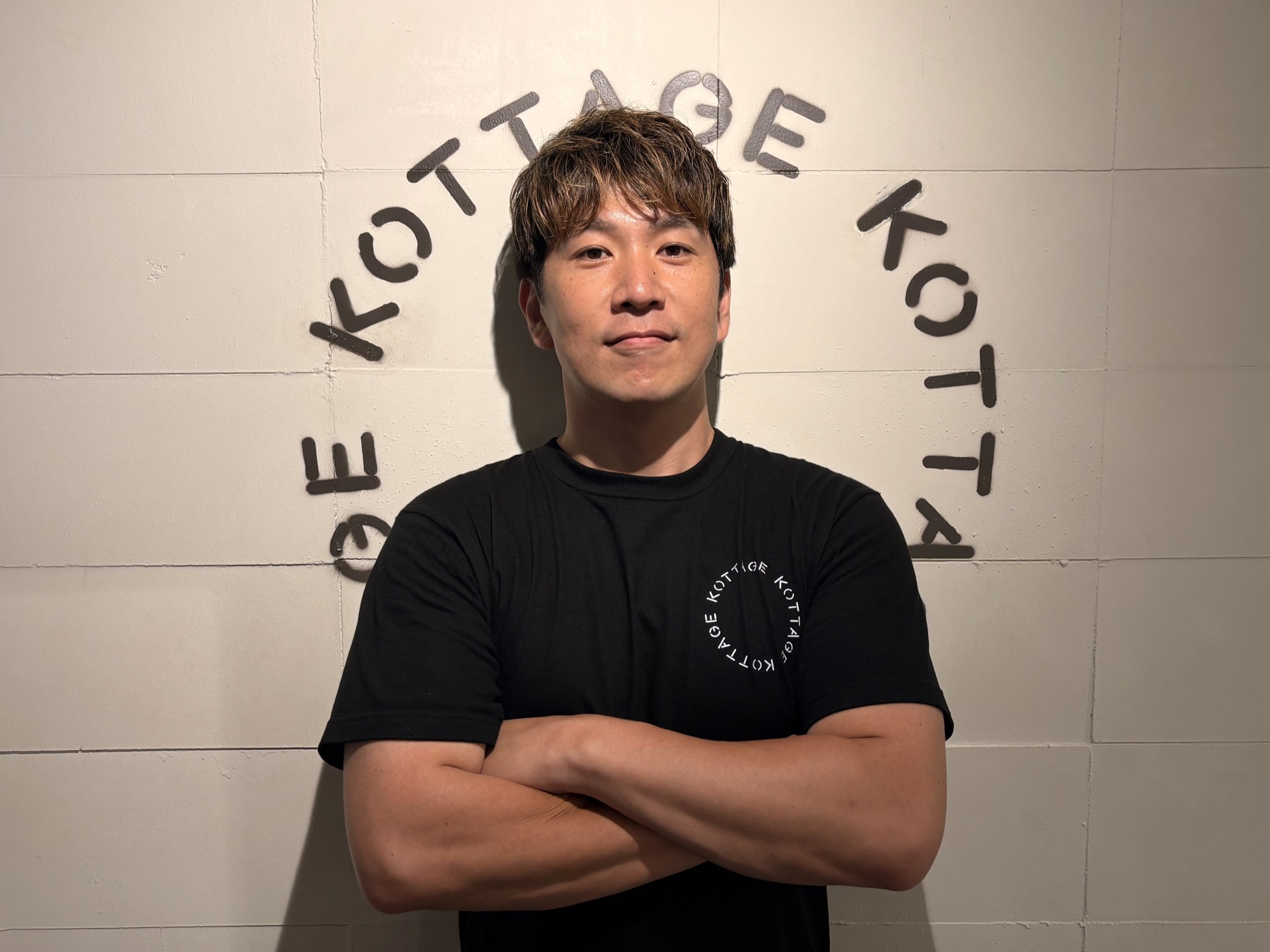 腕を組んで立つKOTTAGE代表のコージ